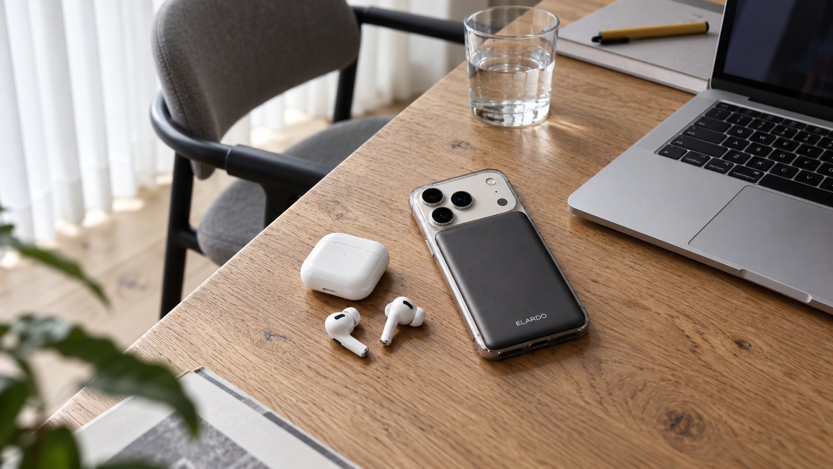 Graphite ELARDO Slim Powerbank on an iPhone next to earbuds on an oak desk